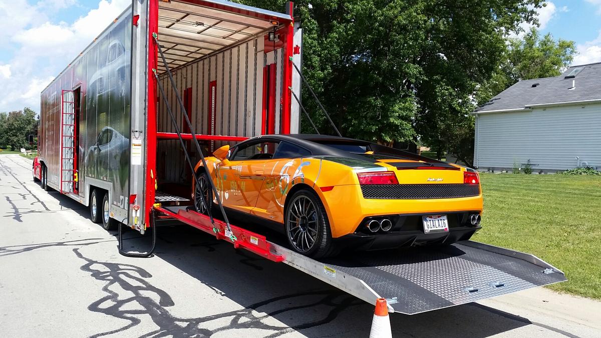 Luxury cars being carefully loaded onto enclosed transport trailer